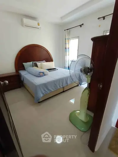 Cozy bedroom with air conditioning and natural light, featuring a comfortable bed and a standing fan.