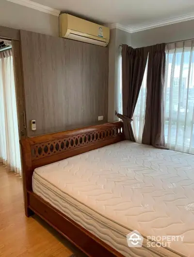 Spacious bedroom with elegant wooden bed frame, large windows draped with curtains, and a cozy ambiance enhanced by natural light.