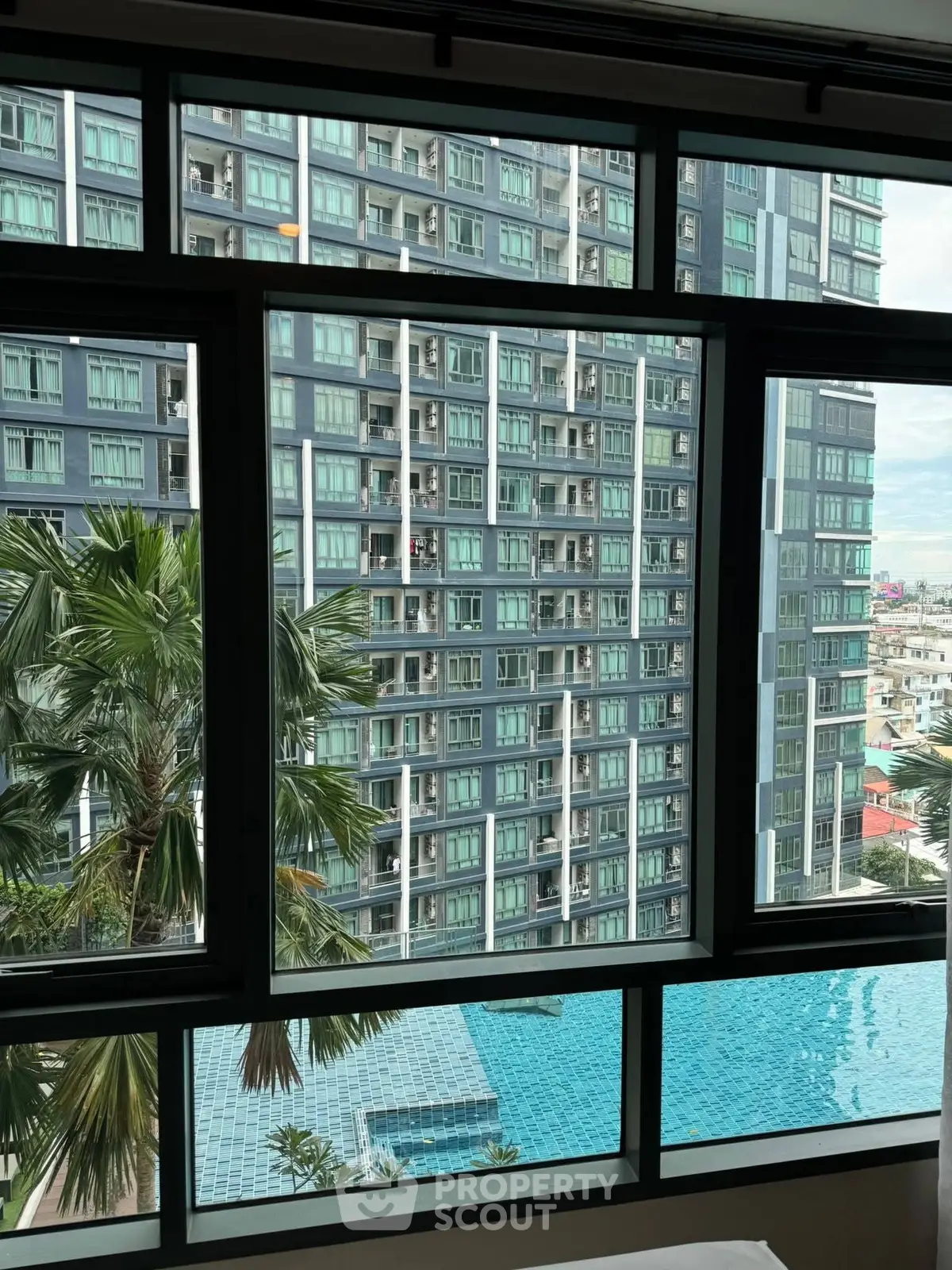 Stunning high-rise view with pool and palm trees from modern apartment window.