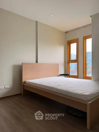 Modern bedroom with wooden flooring and large windows offering city views.