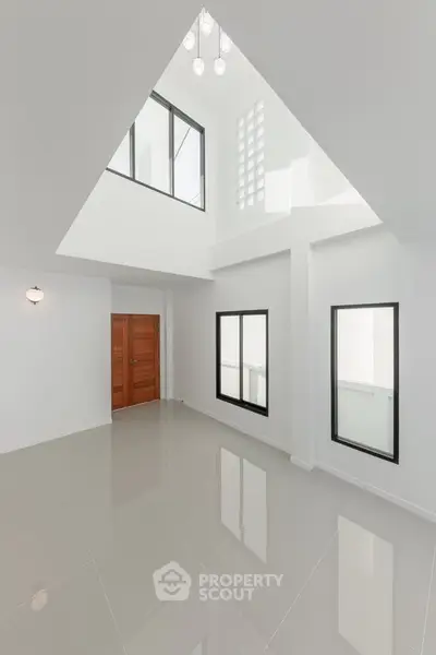 Spacious modern interior with high ceilings and large windows, featuring sleek tile flooring and elegant lighting.