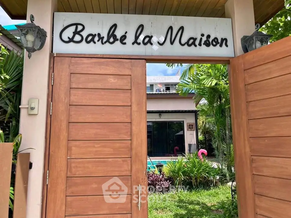 Charming entrance to a tropical home with wooden gate and lush garden, perfect for serene living.