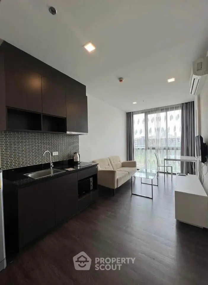 Modern open-layout living room with kitchen, featuring sleek cabinetry and large windows.