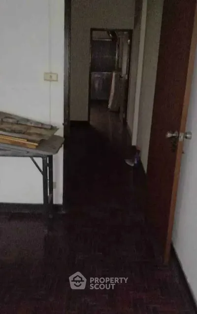 Dimly lit interior hallway with dark wooden flooring and open doors.