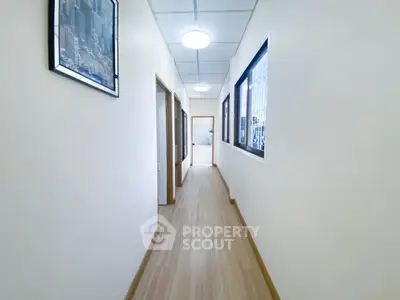 Bright hallway with wooden flooring and framed artwork, leading to multiple rooms.