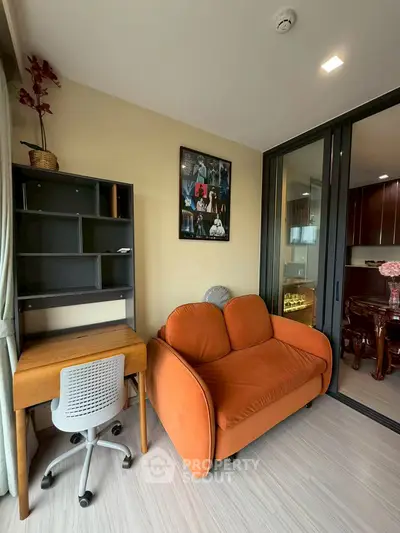 Modern living room with orange sofa and study desk, featuring sliding glass doors to a balcony.