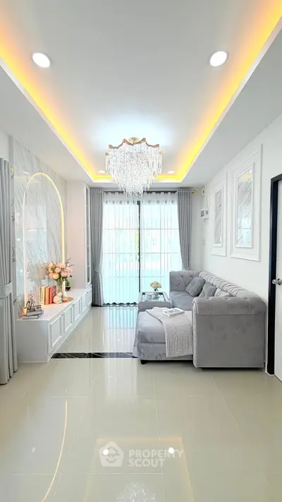 Luxurious living room with elegant chandelier and plush gray sofa in modern apartment.