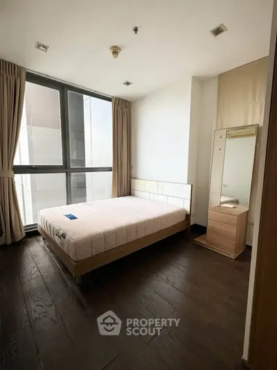 Spacious bedroom with large window and modern furnishings in a high-rise apartment.
