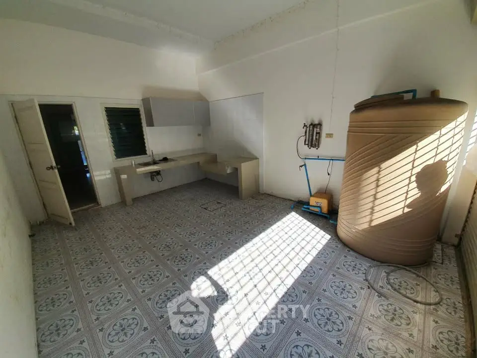 Spacious kitchen area with tiled flooring and large water tank, ideal for renovation.