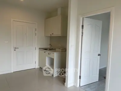 Compact kitchen area in modern apartment with white cabinetry and tiled flooring.