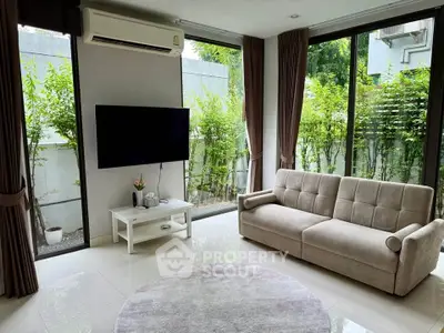 Modern living room with large windows, cozy sofa, and wall-mounted TV overlooking lush greenery.