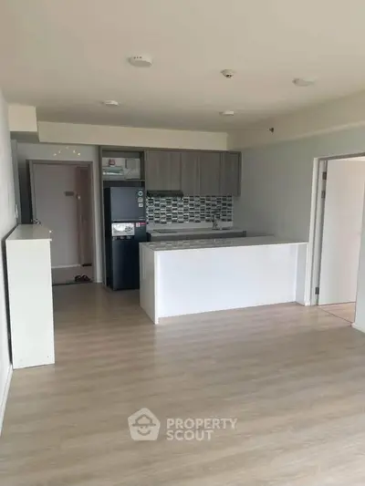 Modern open-plan kitchen with sleek cabinetry and wood flooring in a bright apartment.