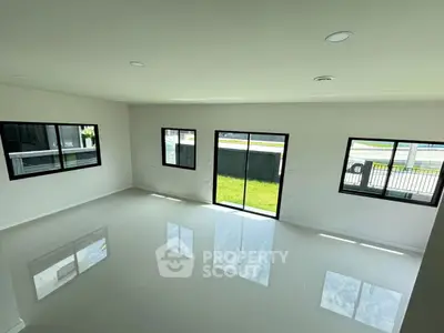 Spacious modern living room with large windows and glossy tile flooring, offering ample natural light.