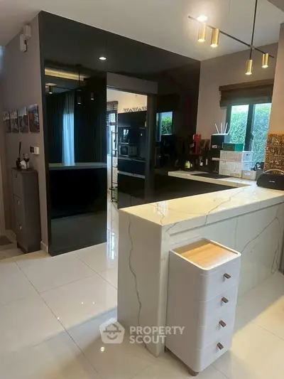 Modern kitchen with sleek black cabinets and marble countertop, featuring open layout and stylish lighting.