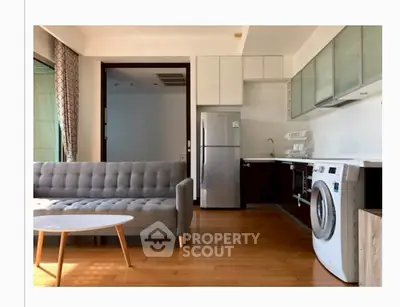 Modern living room with sleek kitchen, washing machine, and stylish sofa in bright natural light.