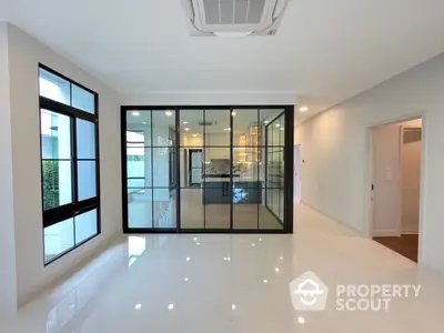 Spacious and modern living area with glossy white tiles, large windows, and a view into a glass-enclosed room, offering a sleek, contemporary living space.