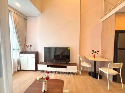 Modern living room with stylish furniture and natural light, featuring a TV and dining area.