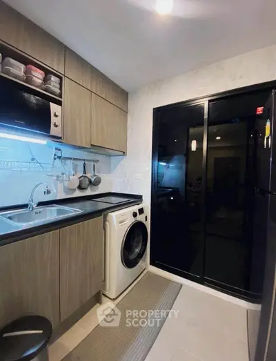 Modern kitchen with sleek cabinetry, washing machine, and microwave, featuring a closed layout and contemporary design.