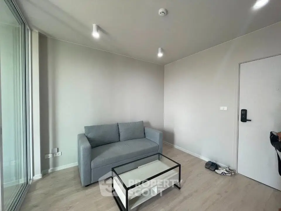 Modern living room with sleek gray sofa and glass coffee table in minimalist apartment.