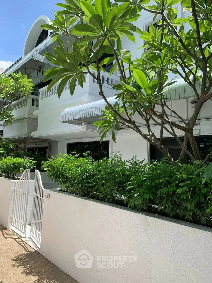 Charming white building with lush greenery and elegant awnings, perfect for serene living.