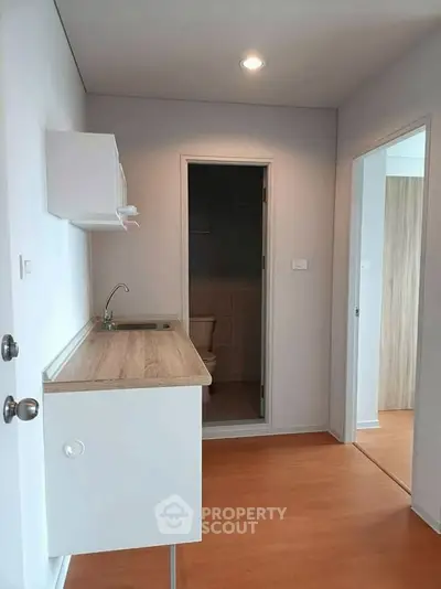 Compact kitchen area with wooden countertop and adjacent bathroom in modern apartment.