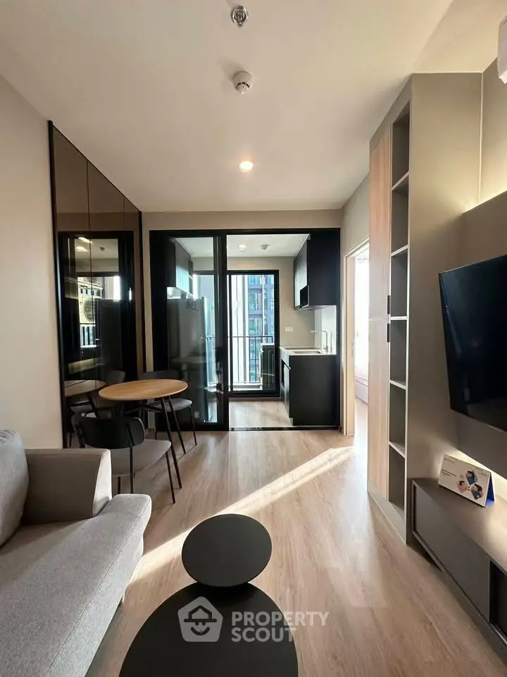 Modern living room with open kitchen and balcony view, featuring sleek furniture and natural light.