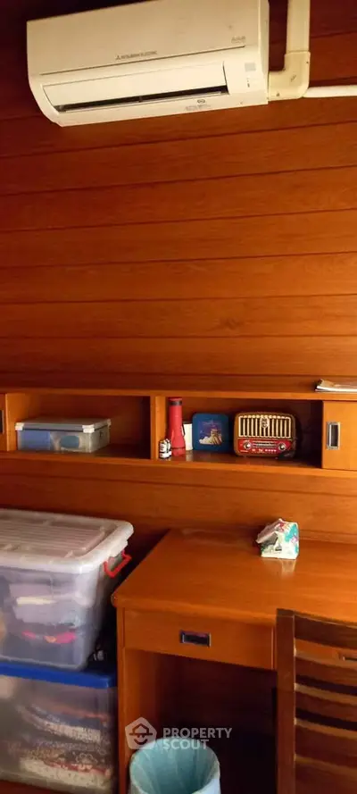 Cozy study room with wooden walls and air conditioning, featuring a desk and storage solutions.