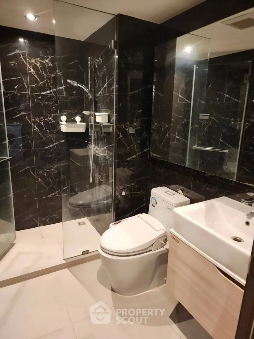 Luxurious modern bathroom with sleek black marble walls and glass shower enclosure.