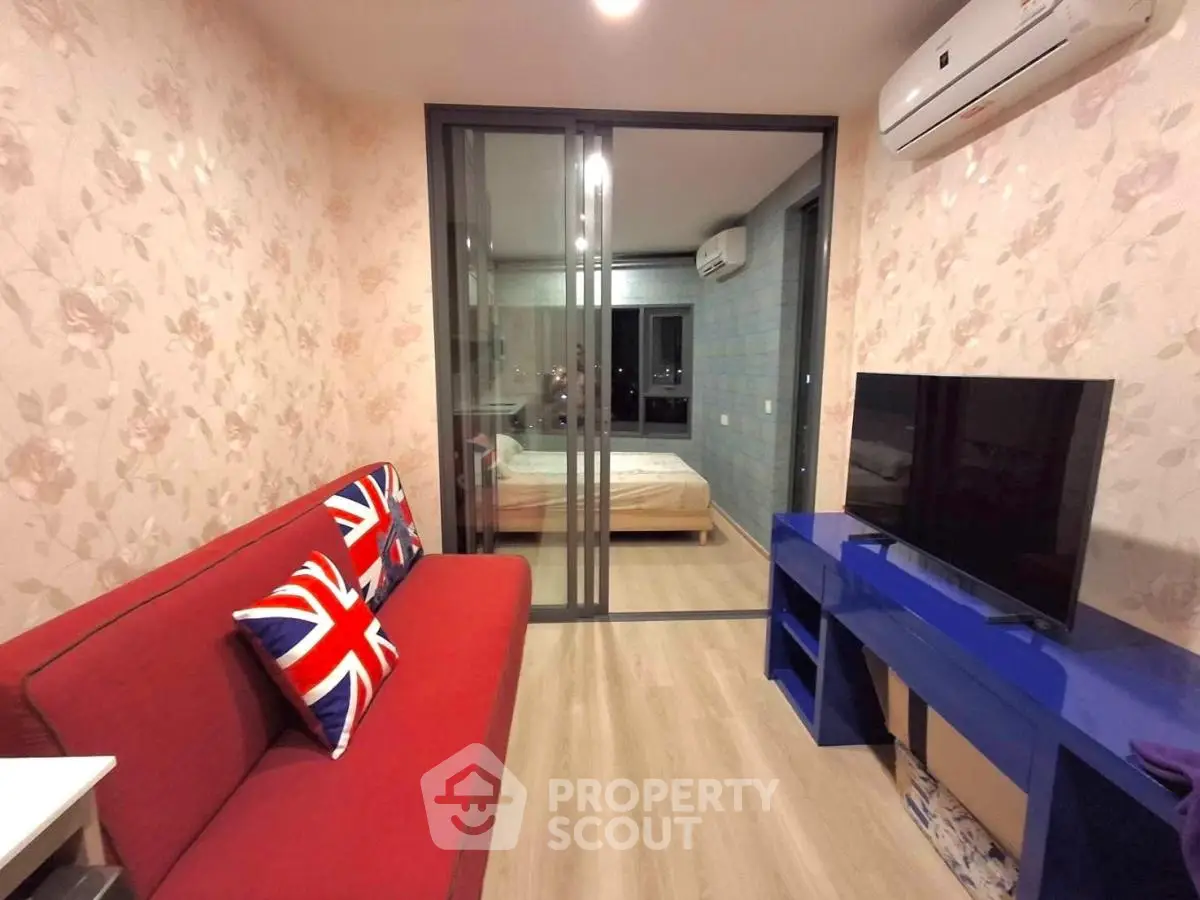 Modern living room with red sofa, TV, and view into bedroom through glass doors.