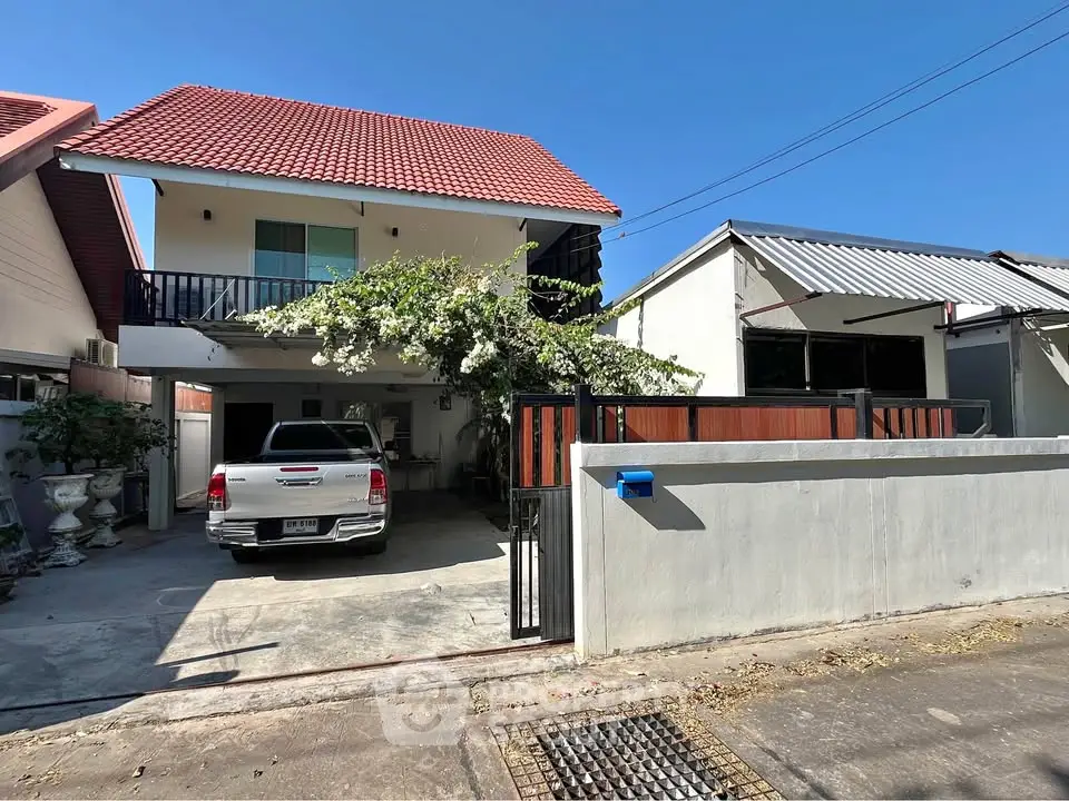 Charming two-story house with red roof, spacious driveway, and lush greenery in a serene neighborhood.