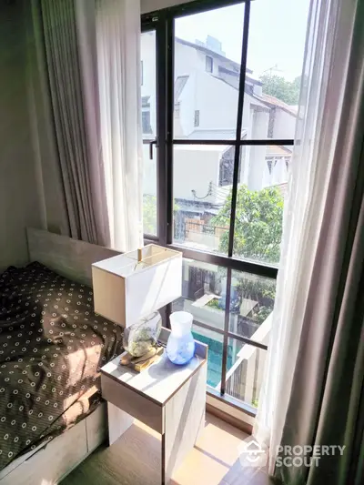 Cozy bedroom corner with a large window offering abundant natural light and a serene view, complemented by sheer curtains and modern decor.