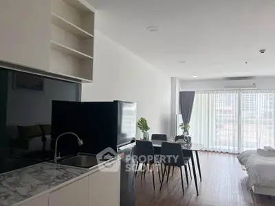 Modern open-plan living room with kitchen and dining area, featuring sleek furniture and large windows.
