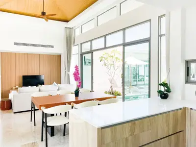 Spacious modern living room with open kitchen and pool view, featuring elegant decor and natural light.