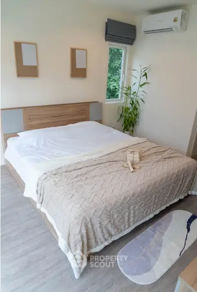 Modern bedroom with cozy bedding and natural light, featuring a stylish plant and air conditioning.