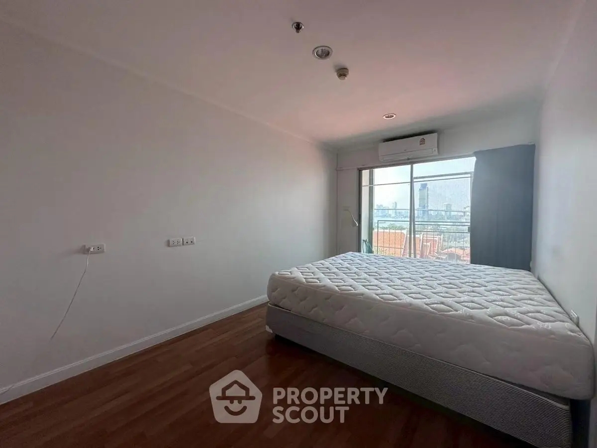 Spacious bedroom with city view and natural light, featuring a comfortable bed and air conditioning.