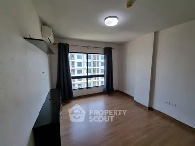 Spacious empty room with large window and wooden flooring in modern apartment.