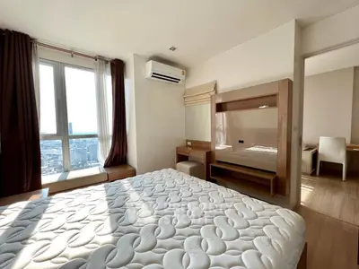 Spacious bedroom with city view and modern furnishings in high-rise apartment.
