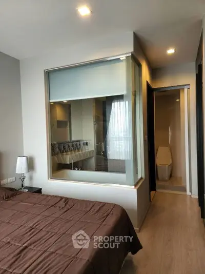 Modern bedroom with ensuite bathroom featuring glass partition and cozy decor.
