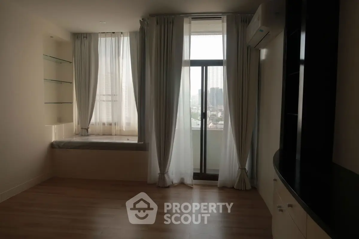 Spacious living room with large windows and city view, featuring elegant curtains and built-in shelves.
