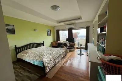 Spacious bedroom with balcony and city view, featuring wooden flooring and modern decor.
