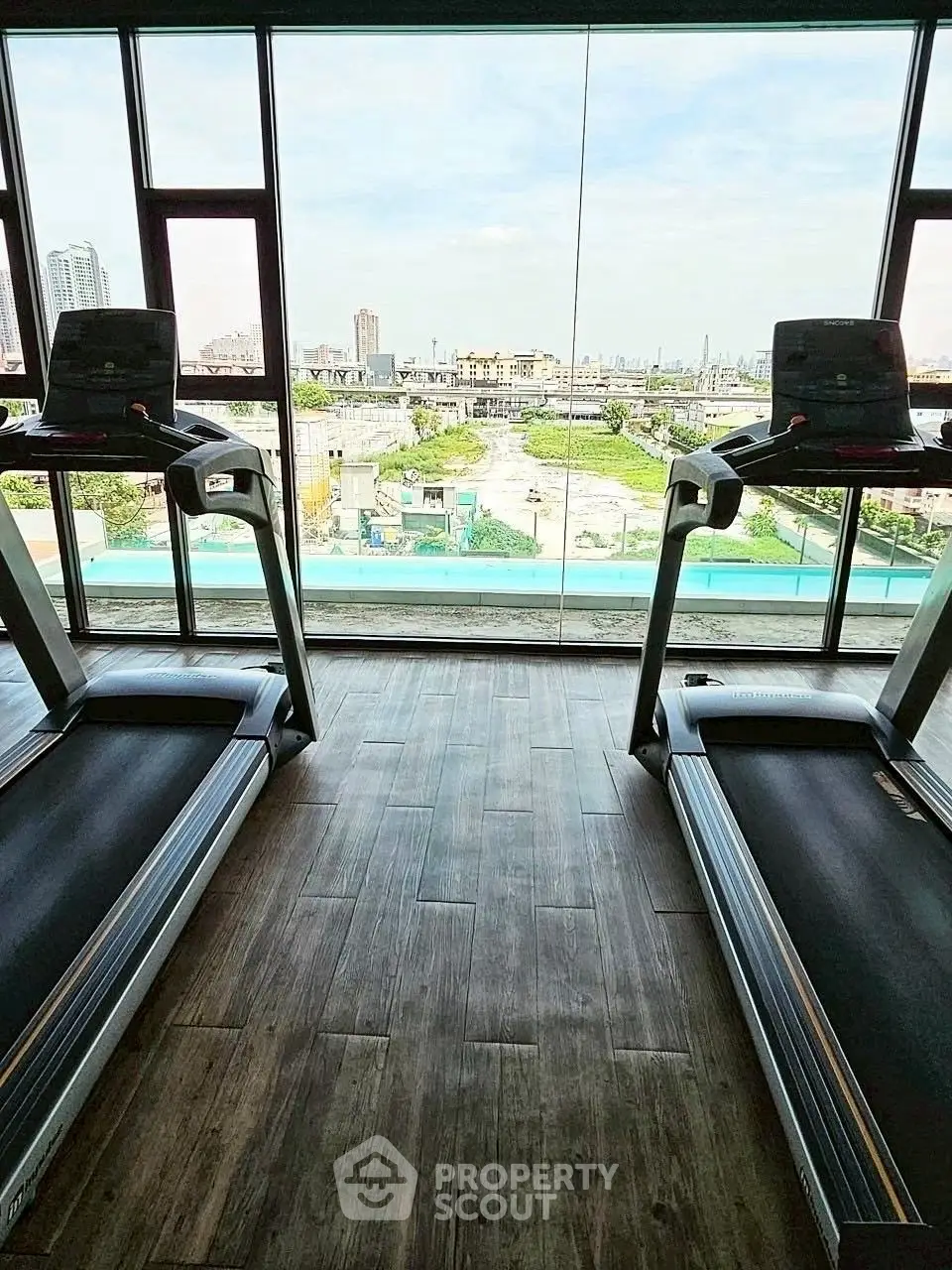Modern gym with treadmills and panoramic city view through large windows.