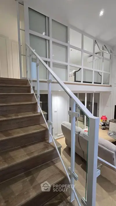 Modern duplex interior with stylish staircase and glass partitions, showcasing open living space.