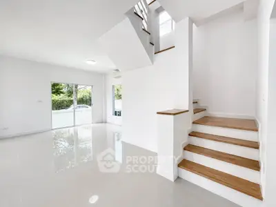 Spacious modern living room with sleek staircase and large windows offering natural light.