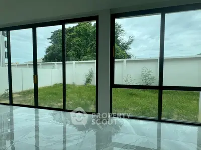 Spacious modern living room with large glass doors opening to a private garden, featuring sleek marble flooring.