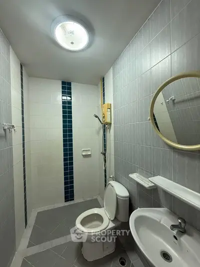 Modern bathroom with sleek design, featuring a round mirror, toilet, and shower area.