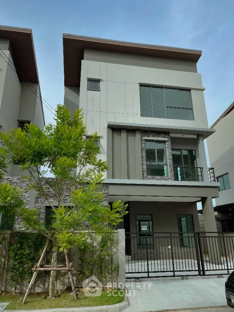 Modern three-story house with sleek design and gated entrance in a serene neighborhood.