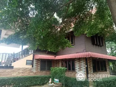 Charming two-story home nestled under lush greenery with a unique brick facade and cozy design, featuring a shaded porch and tranquil surroundings.