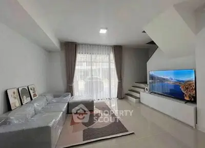 Modern living room with sleek design, large TV, and natural light from window.