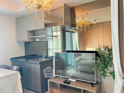 Modern living room with open kitchen, elegant chandelier, and sleek TV setup.
