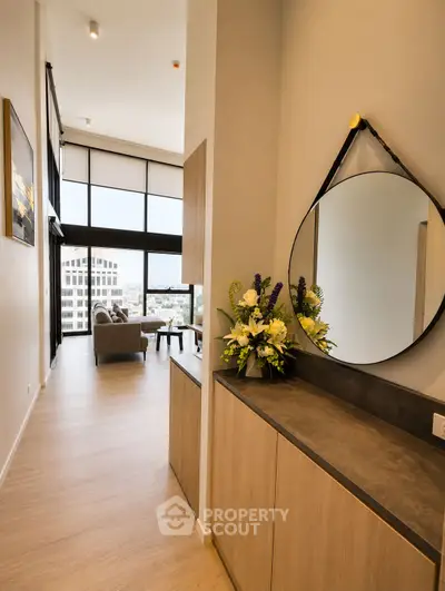 Modern living room with high ceilings and large windows offering city views, featuring stylish decor and a cozy seating area.